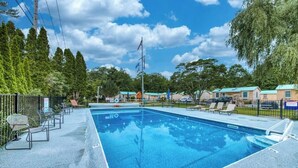 A swimming pool with lounge chairs, a flagpole, and a fenced area with trees.