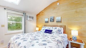 A bedroom with a large bed, a skylight, a wooden headboard, and a nightstand with a lamp.