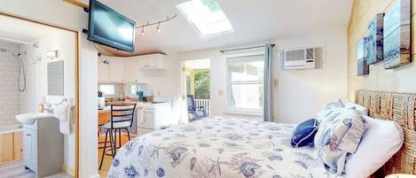 Un dormitorio con cama, televisor, tragaluz, espacio para cocinar y baño.