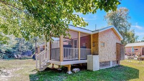A wooden cabin with a porch, a covered deck, and a fenced yard.