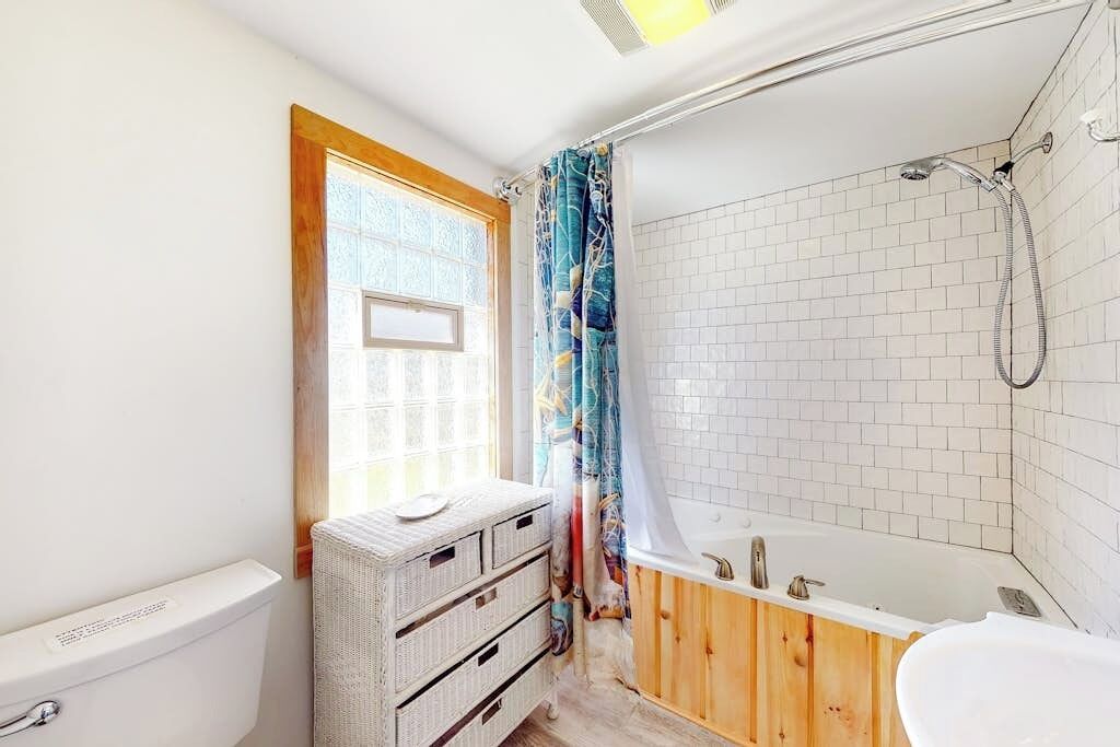 Une salle de bain avec une baignoire, des toilettes et une fenêtre avec un rideau.