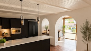 A modern kitchen with dark cabinetry, stainless steel appliances, pendant lighting, and a large island.
