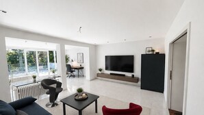 A modern living room with a sofa, a red chair, a coffee table, a TV, and a black cabinet.