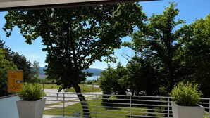 A balcony with a view of a road, trees, and a distant body of water.