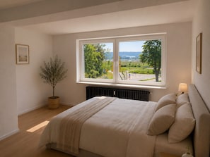 Ein Schlafzimmer mit großem Fenster, einem Bett, einem Heizkörper, einem Topfpflanzen und einer Lampe.