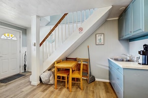 Eine Treppe führt zum Schlafzimmer auf dem Dachboden, einem Essbereich mit Tisch und Stühlen, sowie zu einer Küche mit blauen Schränken. Ein 'Nichtraucher'-Schild ist ebenfalls sichtbar.