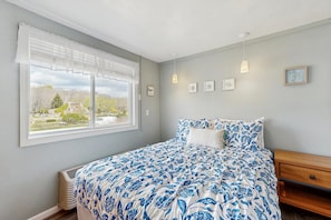 Ein Schlafzimmer mit einem großen Bett, einem Fenster mit Jalousien, einem Nachttisch aus Holz und Wandleuchten.