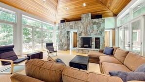 Amplia sala de estar con chimenea de piedra, techo de madera y ventanas grandes.