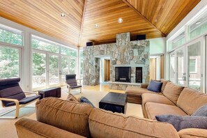 Ein geräumiges Wohnzimmer mit Kamin aus Stein, Holzboden und großen Fenstern.