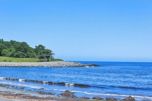 Eine Küstenlandschaft mit felsigem Ufer, ruhiger See und einer grasbewachsenen Fläche mit Bäumen.