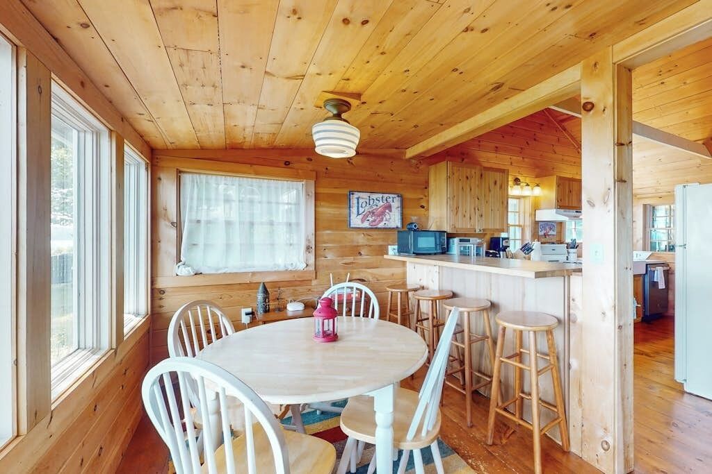 A wooden cabin interior with a dining area, kitchen, and bar.