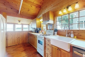 Ein Interieur einer Holzhütte mit einer Küche, die einen Herd, einen Backofen und ein Spülbecken beinhaltet.