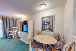 A room with a dining table, chairs, a television, a wardrobe, and a painting on the wall.
