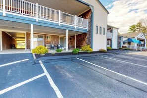 A hotel with a covered outdoor seating area, a parking lot, and a building with a balcony.