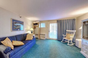 A room with a blue sofa, a rocking chair, a TV, and a window with curtains.