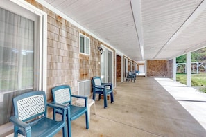 A covered outdoor seating area with chairs and tables, a concrete floor, and a brick wall.
