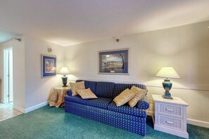 A room with a blue sofa, two side tables with lamps, a framed picture on the wall, and a door.