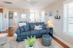 Ein Wohnzimmer mit einer dunkelgrauen Couch, einem kleinen runden Hocker, einer Topfpflanze, einer Lampe und maritimer Dekoration.