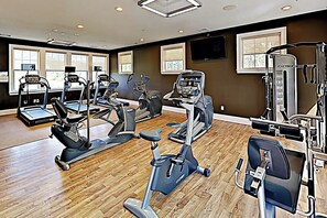 Ein Fitnessstudio mit Cardiogeräten, Krafttrainingsgeräten und einem Fernseher an der Wand.