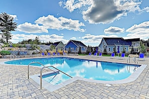 Ein Swimmingpool mit Liegestühlen, einem Kiesweg und Häusern im Hintergrund.