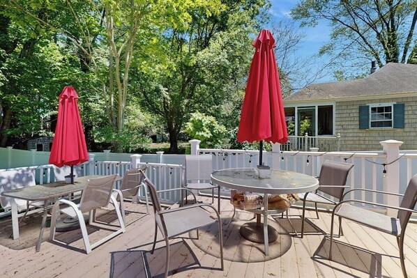 An outdoor patio with round tables and chairs, red umbrellas, and a white fence.