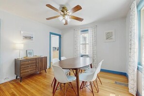 A dining area with a round table, white chairs, a wooden cabinet, and a ceiling fan.