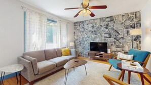 Ein Wohnzimmer mit Sofa, Couchtisch und Sesseln, einer Steinwand, einem Fernseher und einem Deckenventilator.
