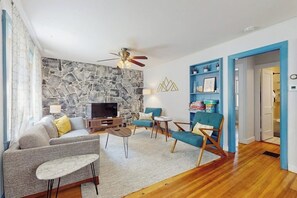 A living room with a stone wall, a ceiling fan, a television, a sofa, a coffee table, and a blue armchair.