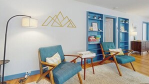 Ein Wohnzimmer mit zwei blauen Sesseln, einem kleinen Tisch, einer Stehlampe und einer blauen Regaleinheit an der Wand.