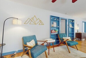 A living room with two blue armchairs, a small table, a floor lamp, and a blue shelving unit against the wall.