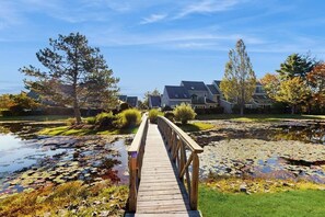 A wooden bridge over a pond with lily pads, surrounded by trees and houses. - Cape Cod style condo with grill, pool, sauna, & gym - near beach (Old Orchard Beach)