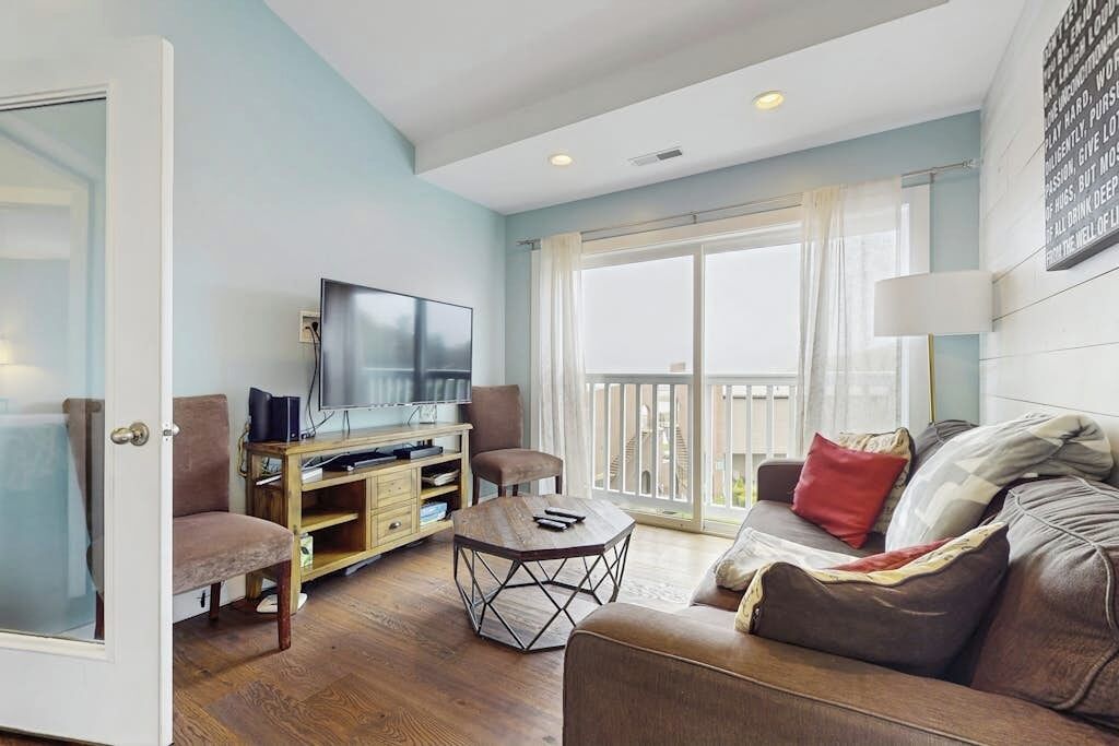 A living room with a TV, wooden entertainment unit, a round coffee table, a sofa, and a balcony with curtains.