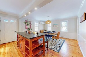 A spacious kitchen with wooden cabinets, a dining area with a patterned rug, and a large window providing natural light. - Idyllic Retreat near the Beach with Fast WiFi, Two Living Areas & Full Kitchen (Kennebunk)