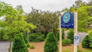 A sign for a hotel with a logo, a contact number, and a trolley stop sign. - Lovely townhome near golf with gas grill, patio, high-speed WiFi, & full kitchen (Ogunquit)