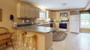 A kitchen with wooden cabinets, a central island with stools, a microwave, a stove, and a refrigerator. - Lovely townhome near golf with gas grill, patio, high-speed WiFi, & full kitchen (Ogunquit)