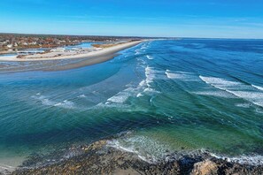 Eine Küstenlandschaft mit Strand, klarem Wasser und einer entfernten Uferlinie mit Gebäuden.