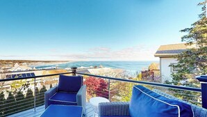 En balkong med blå, vadderade sittplatser, ett litet runt bord och utsikt över havet och byggnaderna.