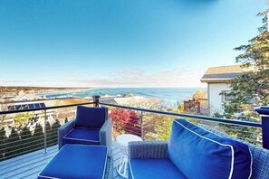 Ein Balkon mit blauen Sitzkissen, einem kleinen runden Tisch und Blick auf das Meer und die Gebäude.