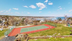 A tennis court with a green and red surface, surrounded by a grassy area and a playground. - Ocean-view condo overlooking Ogunquit Beach with balcony, pool & tennis (Ogunquit)