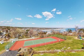 Ein Tennisplatz mit roter und grüner Belag, umgeben von einer Rasenfläche und einem Spielplatz.