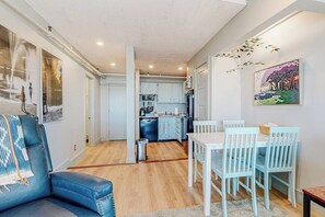 Ein modernes Wohnzimmer mit Sofa, Esstisch und Stühlen, einer Küche im Hintergrund und Kunstwerken an den Wänden.