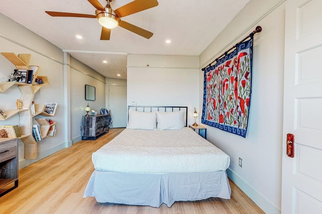 A bedroom with a bed, a ceiling fan, a wall with a patterned tapestry, and built-in shelves.