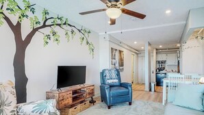 A living room with a TV, a blue chair, a wooden cabinet, and a ceiling fan. - Ocean-view condo overlooking Ogunquit Beach with balcony, pool & tennis (Ogunquit)