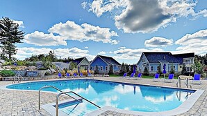 Une piscine avec des chaises longues, une terrasse en pierre et des maisons en arrière-plan.