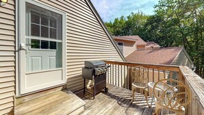 A deck with a grill, outdoor furniture, and a house with a white door and siding. - Riverfront, upstairs studio with fast WiFi & fireplace - dog-friendly (Ogunquit)