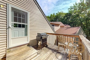 Eine Terrasse mit Grill, Gartenmöbeln und einem Haus mit weißer Tür und Fassade.