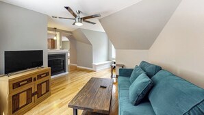 A modern living room with a flat-screen TV, wooden entertainment unit, teal sofa, and a ceiling fan. - Riverfront, upstairs studio with fast WiFi & fireplace - dog-friendly (Ogunquit)