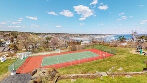 Ein Tennisplatz mit roter und grüner Belag, umgeben von einer Rasenfläche und einem Spielplatz.