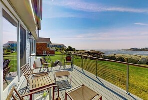 Eine Terrasse mit Sitzgelegenheiten im Freien, Blick auf das Meer und ein Gebäude im Hintergrund.