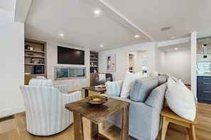 Ein modernes Wohnzimmer mit einer Couch, Sesseln, einem Couchtisch und einem an der Wand montierten Fernseher.